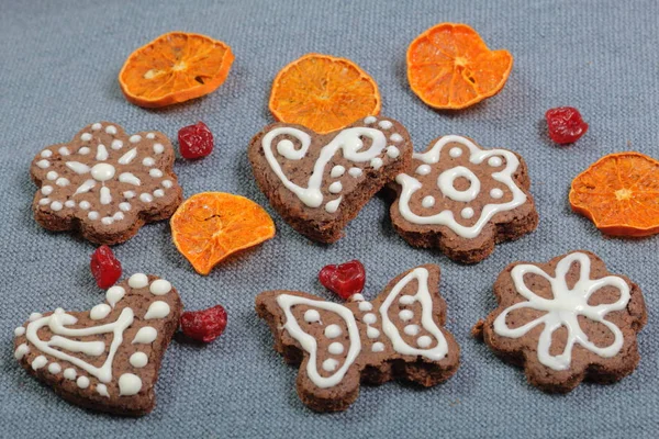 Galletas de jengibre decoradas con un patrón de esmalte blanco. Sobre un fondo de tela gris. Decorado con elementos decorativos de frutos secos — Foto de Stock