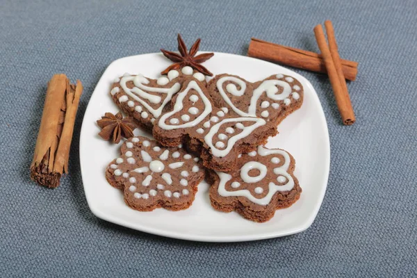 Gingerbread cookies decorated with a pattern of white glaze. On a background of gray fabric. Decorated with decorative elements of cinnamon sticks and anise stars.