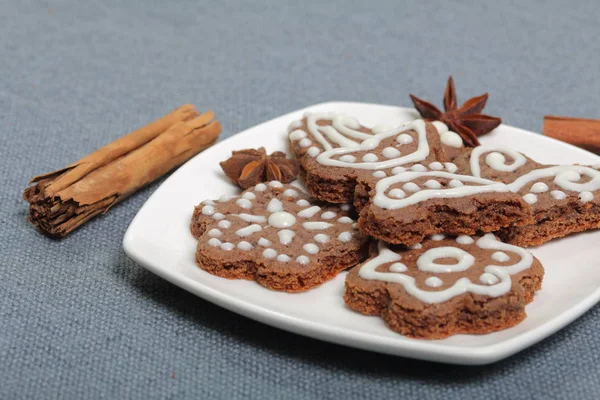 Galletas de jengibre decoradas con un patrón de esmalte blanco. Sobre un fondo de tela gris. Decorado con elementos decorativos de varillas de canela y estrellas de anís . — Foto de Stock