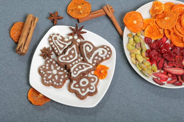 Galletas de jengibre decoradas con un patrón de esmalte blanco. Sobre un fondo de tela gris. Decorado con elementos decorativos de frutas secas, palitos de canela y estrellas de anís . — Foto de Stock