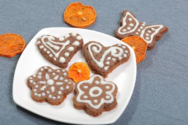 Galletas de jengibre decoradas con un patrón de esmalte blanco. Sobre un fondo de tela gris. Decorado con elementos decorativos de frutos secos — Foto de Stock