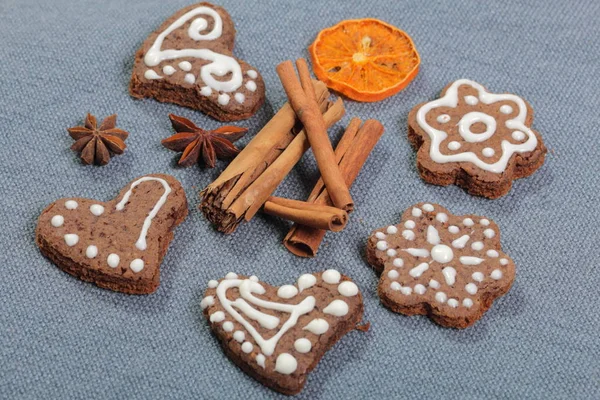 Galletas de jengibre decoradas con un patrón de esmalte blanco. Sobre un fondo de tela gris. Decorado con elementos decorativos de frutas secas, palitos de canela y estrellas de anís . — Foto de Stock