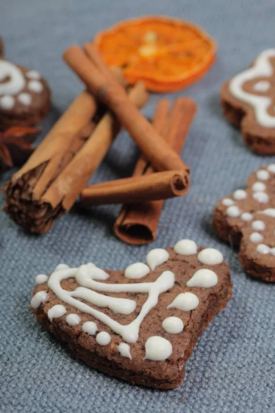 Galletas de jengibre decoradas con un patrón de esmalte blanco. Sobre un fondo de tela gris. Decorado con elementos decorativos de frutas secas, palitos de canela y estrellas de anís . — Foto de Stock