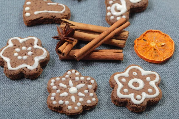 Galletas de jengibre decoradas con un patrón de esmalte blanco. Sobre un fondo de tela gris. Decorado con elementos decorativos de frutas secas, palitos de canela y estrellas de anís . — Foto de Stock