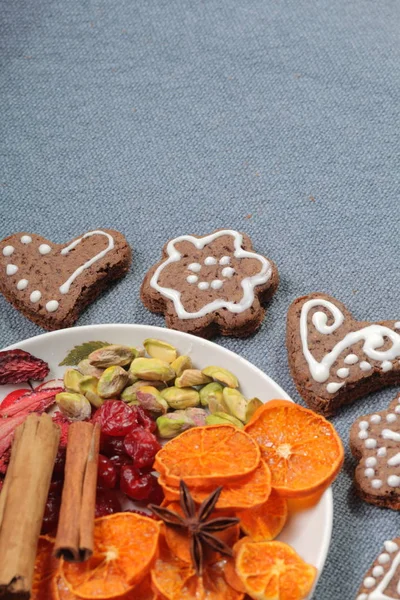 Galletas de jengibre decoradas con un patrón de esmalte blanco. Sobre un fondo de tela gris. Decorado con elementos decorativos de frutas secas, palitos de canela y estrellas de anís . — Foto de Stock