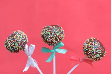 Renkli sprinkles ile çikolata Kek Pops. Kurdele yayı ile dekore edilmiştir. Kırmızı arka planda