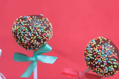 Renkli sprinkles ile çikolata Kek Pops. Kurdele yayı ile dekore edilmiştir. Kırmızı arka planda