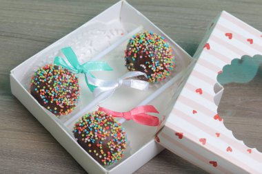Renkli sprinkles ile çikolata Kek Pops. Kurdele yayı ile dekore edilmiştir. Bir hediye kutusunda yatıyorlar, şeffaf bir pencerenin kapağında..