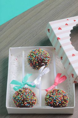 Renkli sprinkles ile çikolata Kek Pops. Kurdele yayı ile dekore edilmiştir. Bir hediye kutusunda yatıyorlar, şeffaf bir pencerenin kapağında..