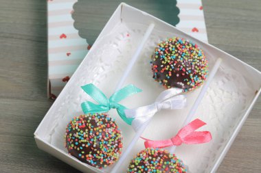 Renkli sprinkles ile çikolata Kek Pops. Kurdele yayı ile dekore edilmiştir. Bir hediye kutusunda yatıyorlar, şeffaf bir pencerenin kapağında..