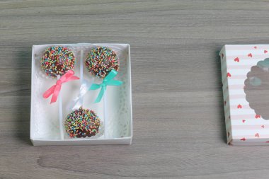 Renkli sprinkles ile çikolata Kek Pops. Kurdele yayı ile dekore edilmiştir. Bir hediye kutusunda yatıyorlar, şeffaf bir pencerenin kapağında..