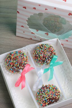 Renkli sprinkles ile çikolata Kek Pops. Kurdele yayı ile dekore edilmiştir. Bir hediye kutusunda yatıyorlar, şeffaf bir pencerenin kapağında..