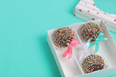 Renkli sprinkles ile çikolata Kek Pops. Kurdele yayı ile dekore edilmiştir. Şeffaf bir pencerenin kapağında bir hediye kutusunda yatıyorlar. Nane arka planında.