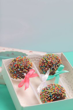 Renkli sprinkles ile çikolata Kek Pops. Kurdele yayı ile dekore edilmiştir. Bir hediye kutusunda yatıyorlar, şeffaf bir pencerenin kapağında..