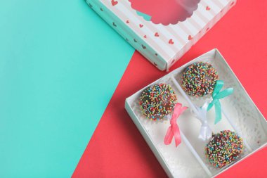 Renkli sprinkles ile çikolata Kek Pops. Kurdele yayı ile dekore edilmiştir. Şeffaf bir pencerenin kapağında bir hediye kutusunda yatıyorlar. Kırmızı ve naneli arka planda.