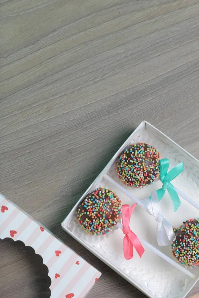 Pastel Pops en chocolate con chispas de colores. Decorado con un lazo de cinta. Se encuentran en una caja de regalo, en la tapa de la que hay una ventana transparente . — Foto de Stock