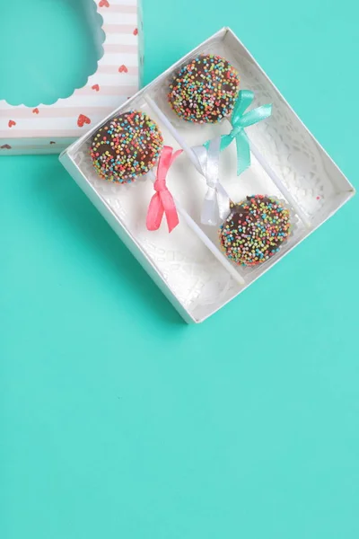 Pastel Pops en chocolate con chispas de colores. Decorado con un lazo de cinta. Se encuentran en una caja de regalo, en la tapa de la cual hay una ventana transparente. Sobre un fondo de menta . — Foto de Stock