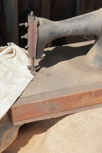 Starý šicí stroj s ručním pohonem. Pokrytý korozí, prachem a pavučinami. Do ní je našitý kus hrubé tkaniny. — Stock fotografie
