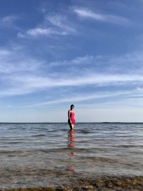 Kız gölün kıyılarında sığ sularda suyun içinden yürüyor. Görünür berrak su ve güzel mavi gökyüzü.