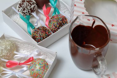 Kek bir hediye kutusuna paketlenmiş, örgü bir yay ile süslenmiş açılır. Yakınlarda eritilmiş çikolata bardakları var..