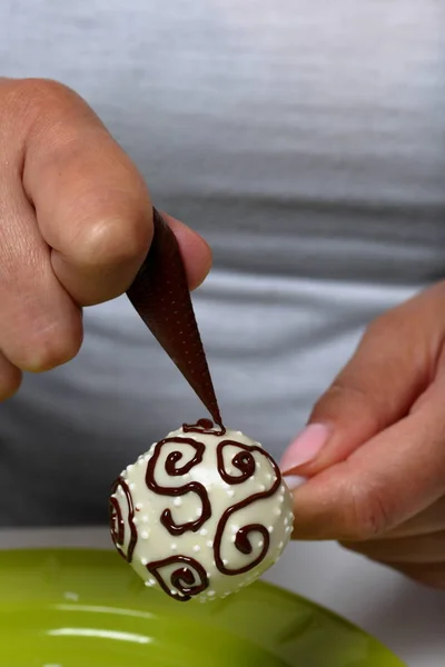 女性は、ホワイトチョコレートでガラス張りのダークチョコレートポップケーキの助けを借りて飾ります. — ストック写真