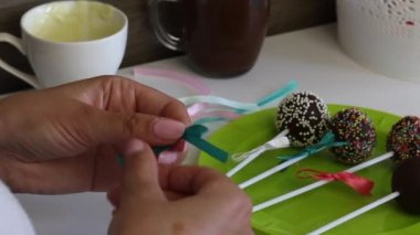 Bir kadın bir tabak üzerinde yatan örgü pasta pops yay süsler. Farklı renklerde saçılma ile süslenmiş şeker..