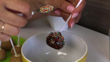 Bir kadın renkli sos ile siyah çikolata popcake kek serpin. Masada sonraki pasta pops için boşluklar vardır.