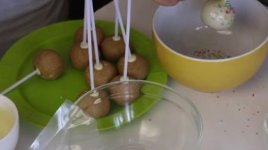 Bir kadın renkli bir sos beyaz çikolata ile popcake serpiştirir. Sonraki masada popcakes yapmak için malzemeler vardır.