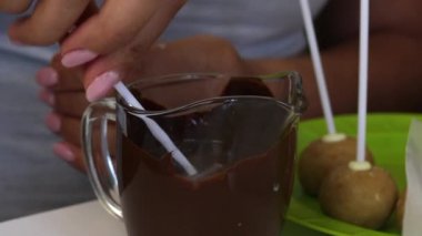 Kadın siyah çikolataya haşhaşlı kek batırıyor. Masanın üstünde pasta çubukları var..