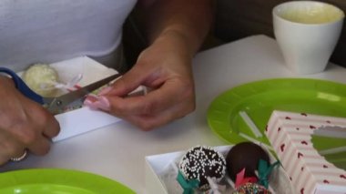 Kadın pasta çubuklarını hediye kutusuna koyuyor. Şekerler farklı renkte sargı ve kurdele ile süslenir. Kesme makasını aşar.