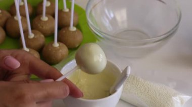 Bir kadın erimiş beyaz çikolata içine bir popcake kütük daldırma. Sırı eşit olarak yayır.