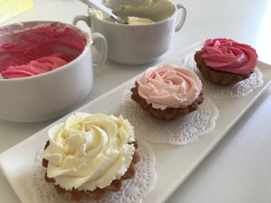 Pasta sepeti. Krem peynir gülleri ile dekore edilmiştir. Dikdörtgen beyaz bir tabağa yığılmış. Dekorasyon için krem ile fincan yakınında. Yukarıdan görüntüle.