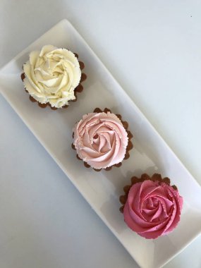 Pasta sepeti. Krem peynir gülleri ile dekore edilmiştir. Dikdörtgen beyaz bir tabağa yığılmış. Yukarıdan görüntüle.