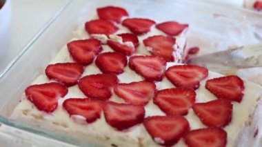 Bir kadın bisküvi, ekşi krema ve çilek katmanları ile hafif ve narin bir pasta keser. Bir tabağa bir parça koyar.