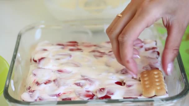 女性は ガラスの形でケーキの上にイチゴのスライスのサワークリームの上にビスケットの層を敷設しています ビスケット サワークリーム イチゴの層と軽く繊細なケーキを準備します — ストック動画