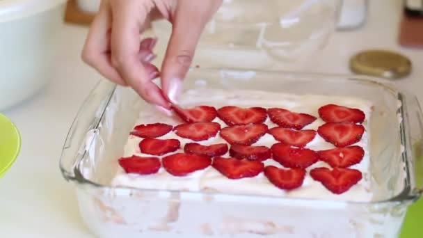 女性は ガラスの形でサワークリームケーキを塗ったイチゴのスライスを置きます ビスケット サワークリーム イチゴの層と光と繊細なケーキを調理 — ストック動画