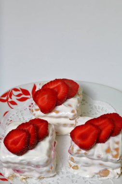 Bisküvi, ekşi krema ve çilek kek. Çilek dilimleri ile dekore edilmiştir. Bir tabak üzerinde yalan.