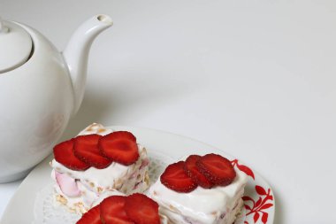 Bisküvi, ekşi krema ve çilek kek. Çilek dilimleri ile dekore edilmiştir. Yakınlarda bir çaydanlık var..