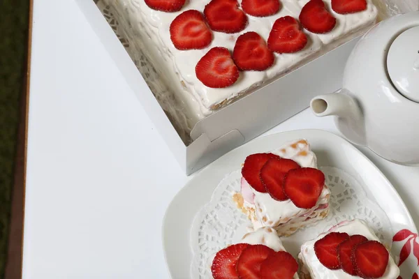 Pastel de galletas, crema agria y fresas. Decorado con rodajas de fresa. Cerca de la misma bollería y tetera . — Foto de Stock