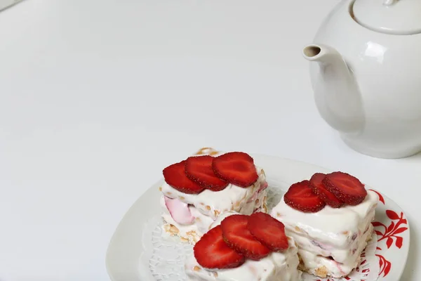 Pasteles de galletas, crema agria y fresas. Decorado con rodajas de fresa. Cerca hay una tetera . — Foto de Stock