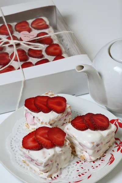 Τούρτα από μπισκότα, ξινή κρέμα και φράουλες. Διακοσμημένο με φέτες φράουλας. Κοντά στα ίδια αρτοσκευάσματα και τσαγιέρα. — Φωτογραφία Αρχείου
