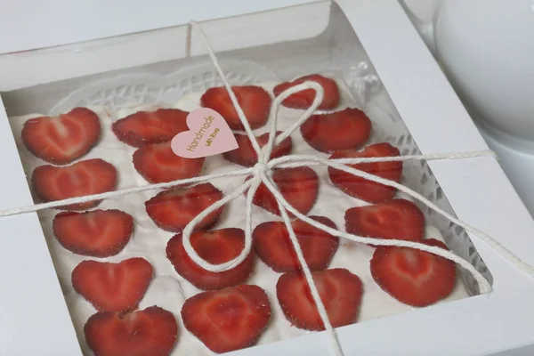 Gâteau de biscuits, crème sure et fraises dans une boîte avec un couvercle transparent. Décoré avec des tranches de fraise. La boîte est reliée avec une corde, et il y a un autocollant sur la boîte . — Photo