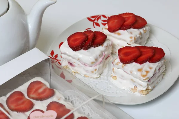 Kaka från kakor, gräddfil och jordgubbar. Dekorerad med jordgubbs skivor. Nära samma bakverk och tekanna. — Stockfoto