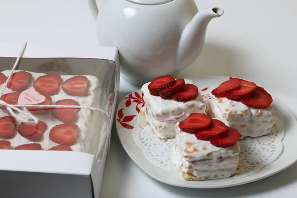 Τούρτα από μπισκότα, ξινή κρέμα και φράουλες. Διακοσμημένο με φέτες φράουλας. Κοντά στα ίδια αρτοσκευάσματα και τσαγιέρα. — Φωτογραφία Αρχείου