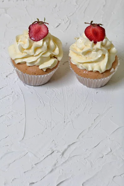 Cupcakes with strawberries and butter cream. On a white surface with decorative plaster. — Stock Photo, Image