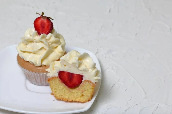 Cupcakes with strawberries and butter cream. One of them is cut, the filling is visible. On a white surface with decorative plaster. — Stock Photo, Image