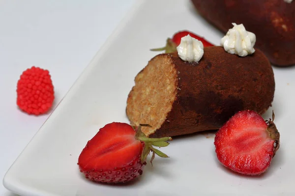 Potato cake decorated with cream. Visible slice of cake. Nearby are the halves of strawberries and colored berries for decoration.