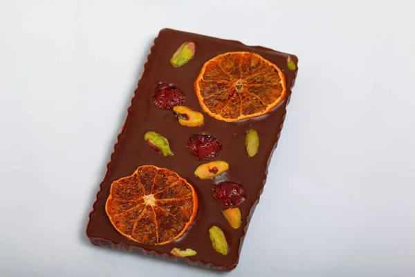 Homemade black chocolate. Decorated with slices of dried orange, strawberries, cherries and pistachios. On a white background.