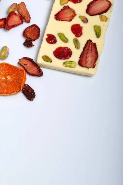 Homemade white chocolate. Decorated with slices of dried orange, strawberries, cherries and pistachios. On a white background.