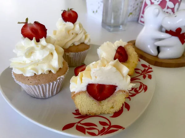 Cupcakes with strawberries and butter cream. One of them is cut, the filling is visible. On a white surface with decorative plaster. — Stock Photo, Image